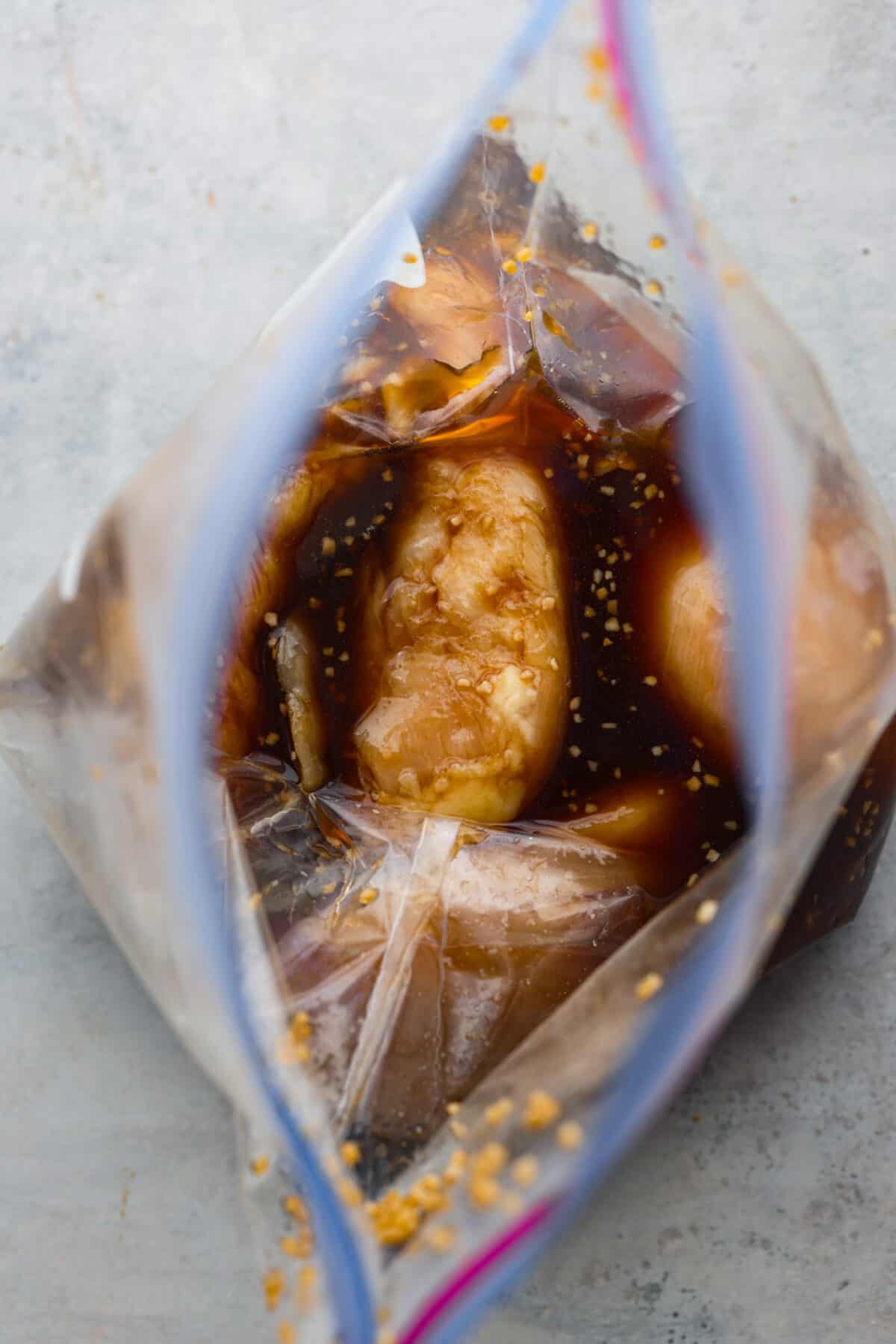 Top-down view of marinating chicken breasts in a ziploc bag.