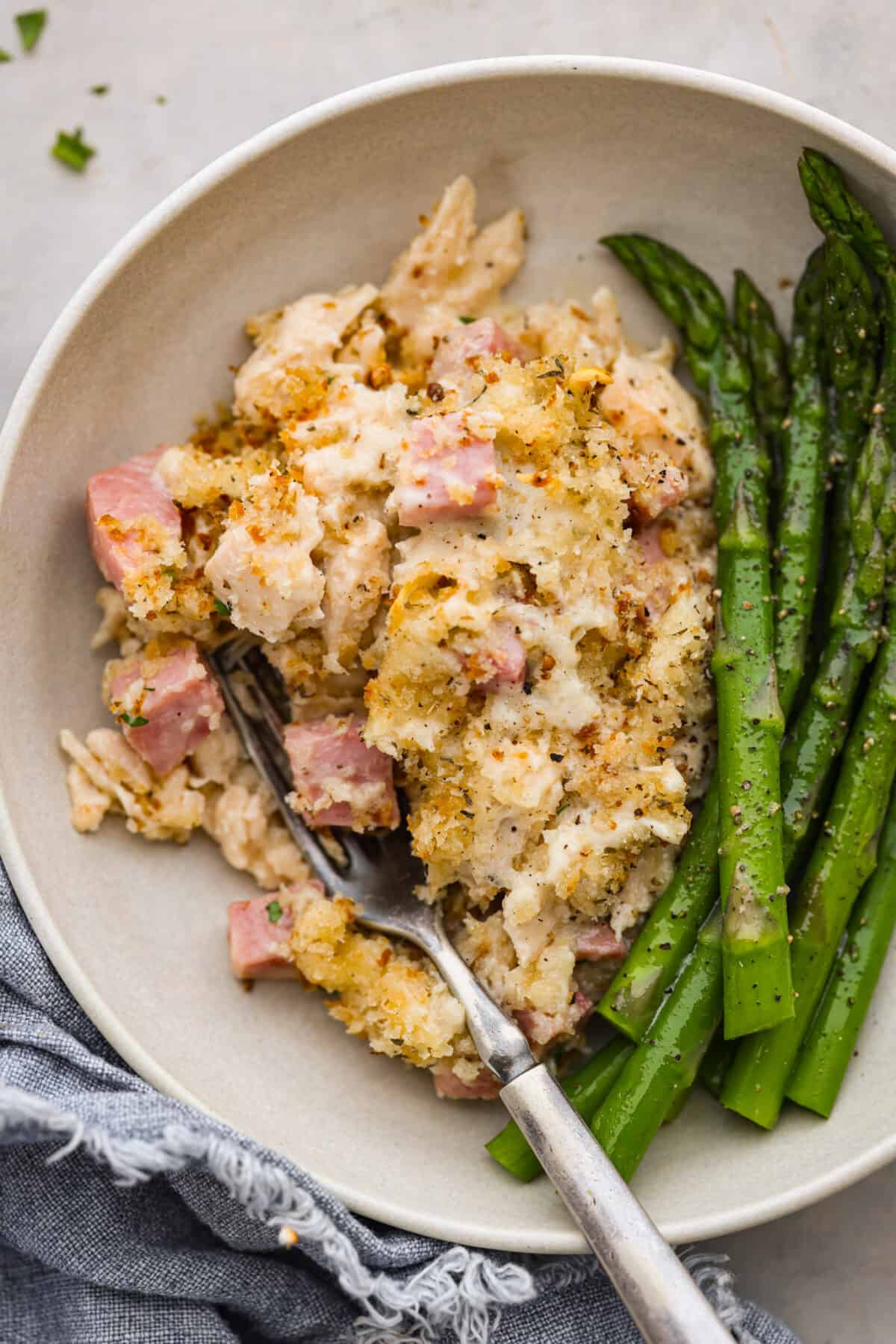 A scoop of the casserole served with asparagus in a cream-colored dish.