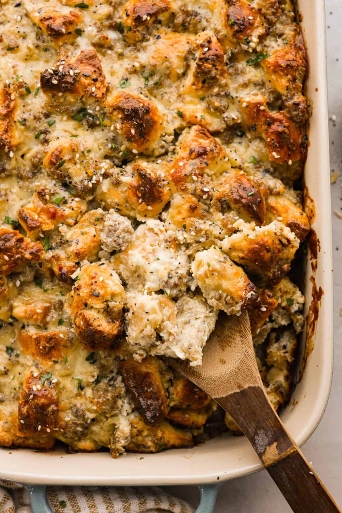 Close view of a wood spoon lifting up everything bagel casserole from the baking dish.