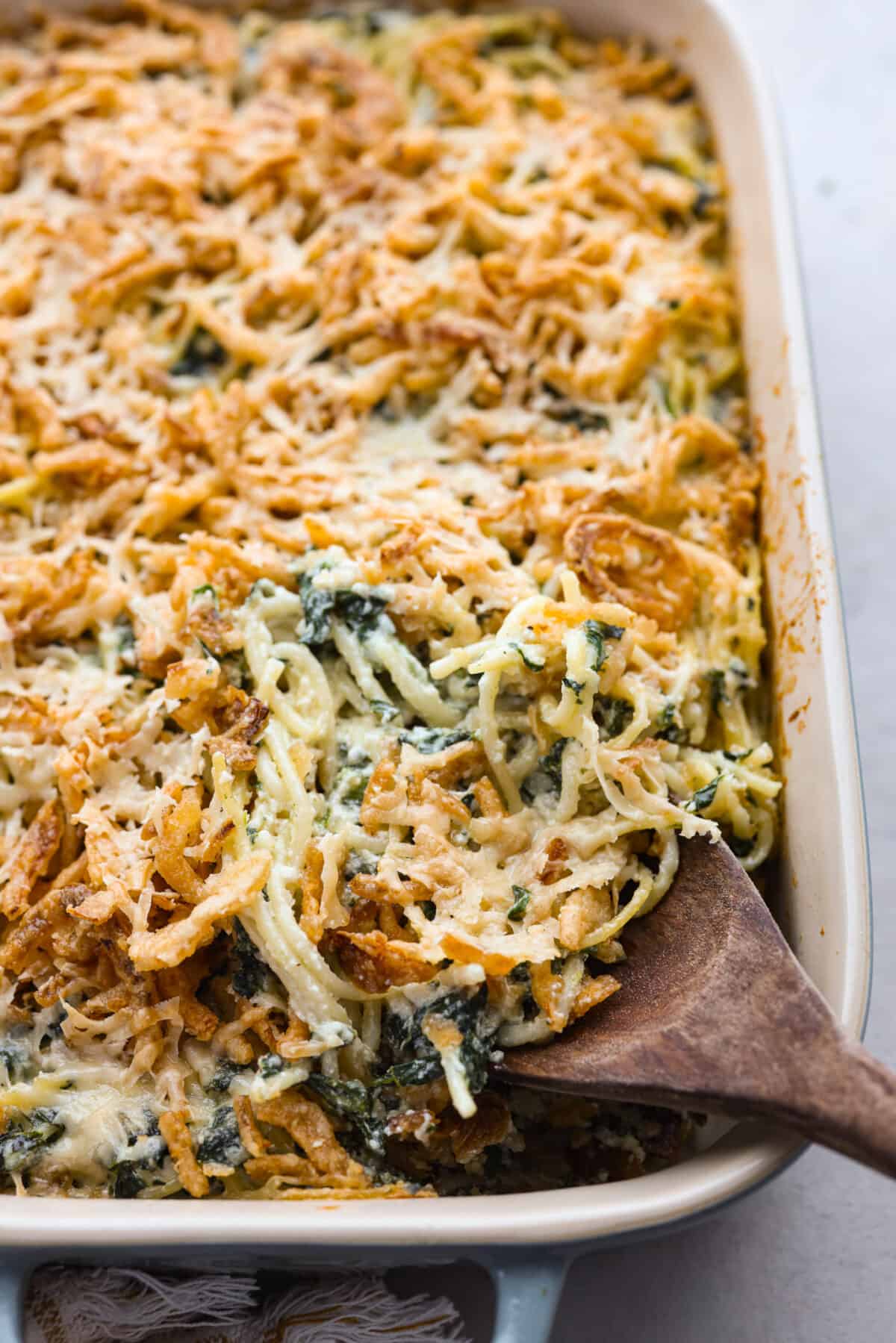 Close view of Monterey spaghetti in a baking dish with a wooden serving spoon.