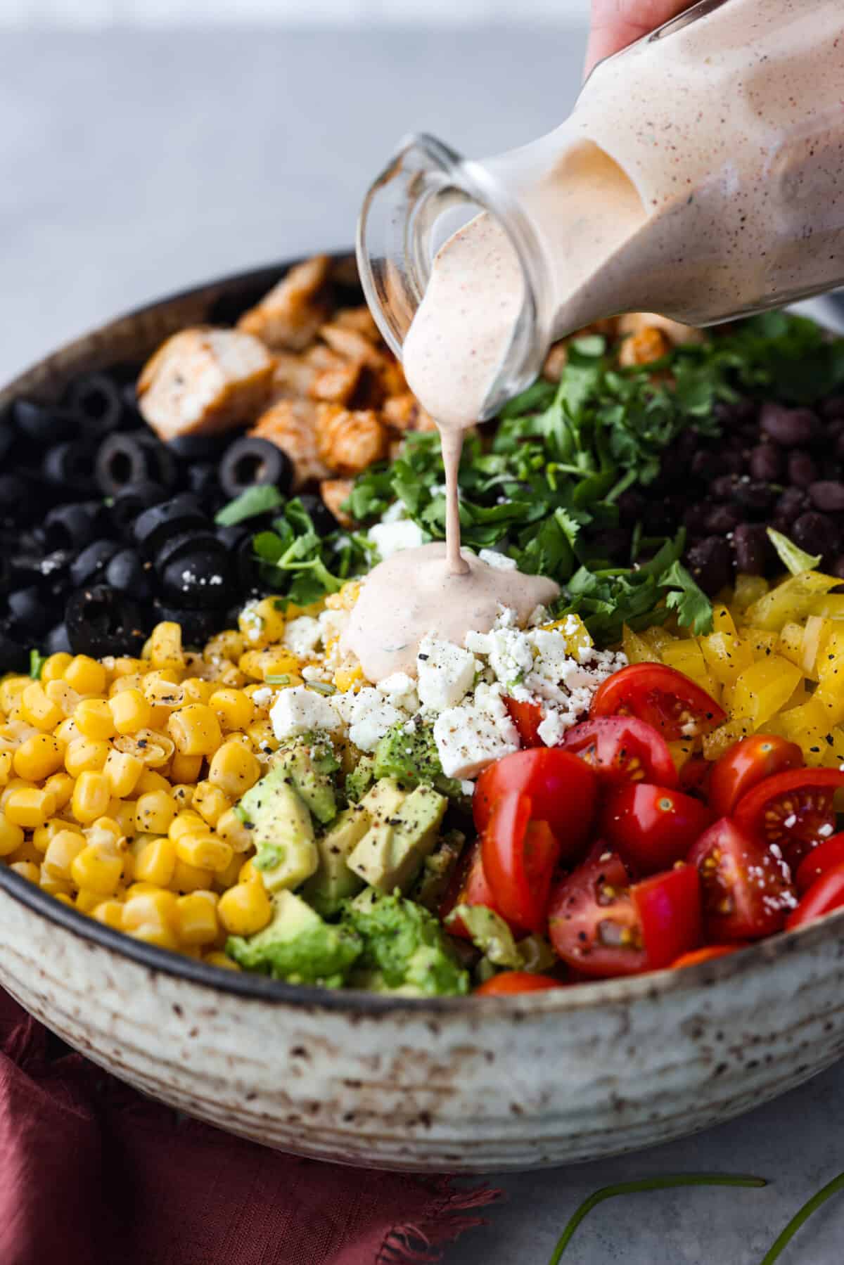 Pouring the southwest sauce over a bowl of greens, corn, olives, and other chopped veggies.