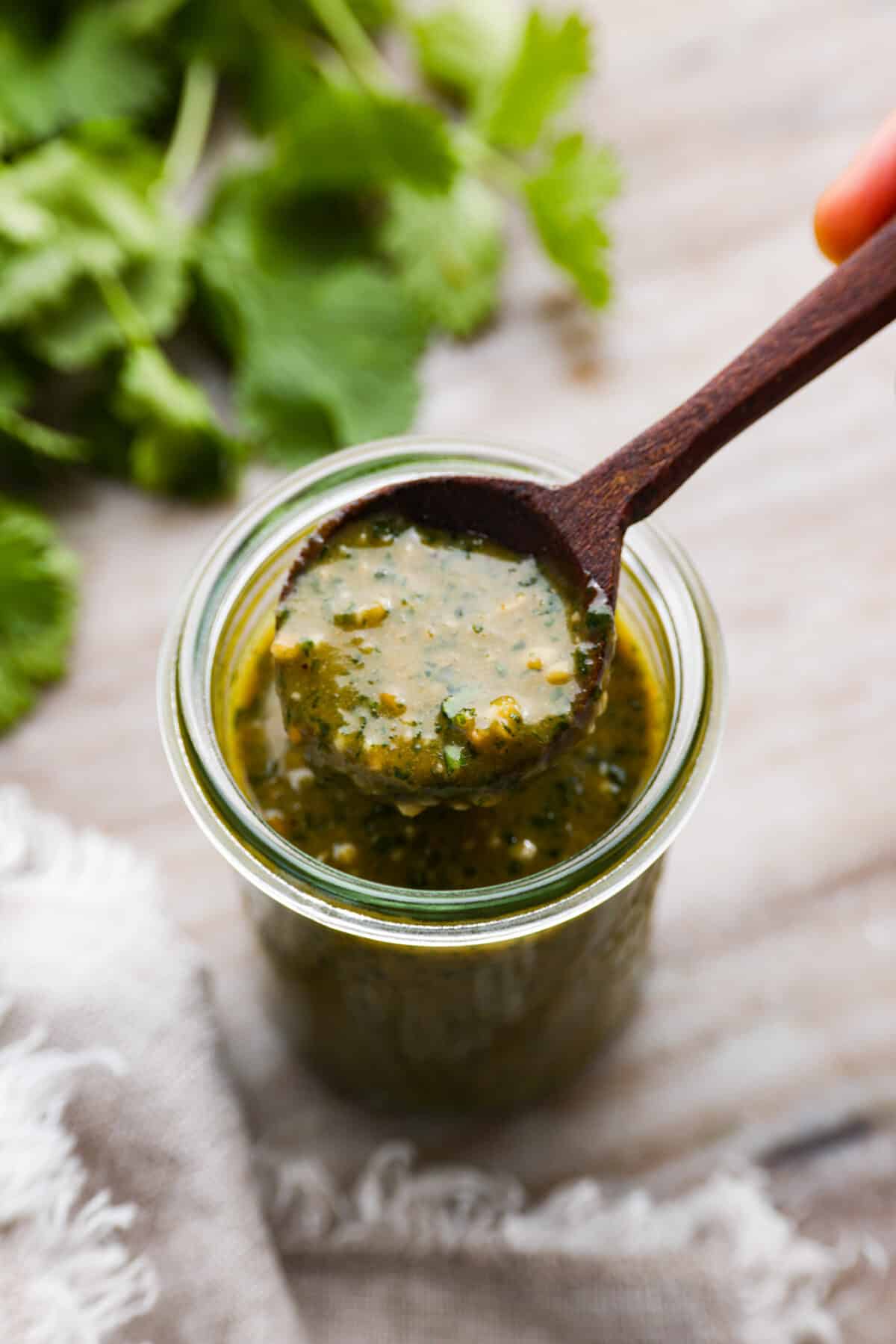 Tamarind cashew dipping sauce in a glass jar, being scooped up with a wooden spoon.