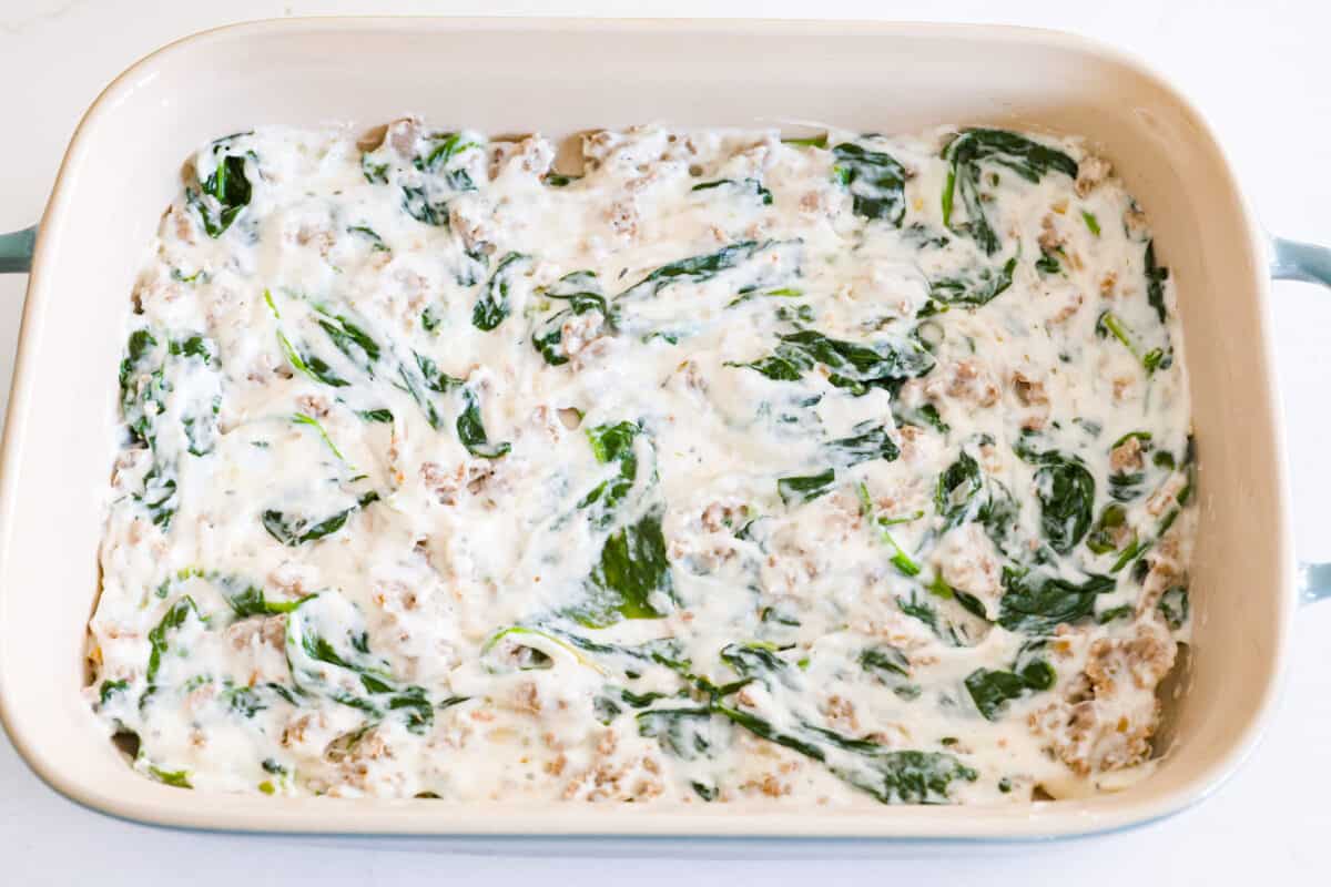 Adding the white sauce layer to a baking dish.