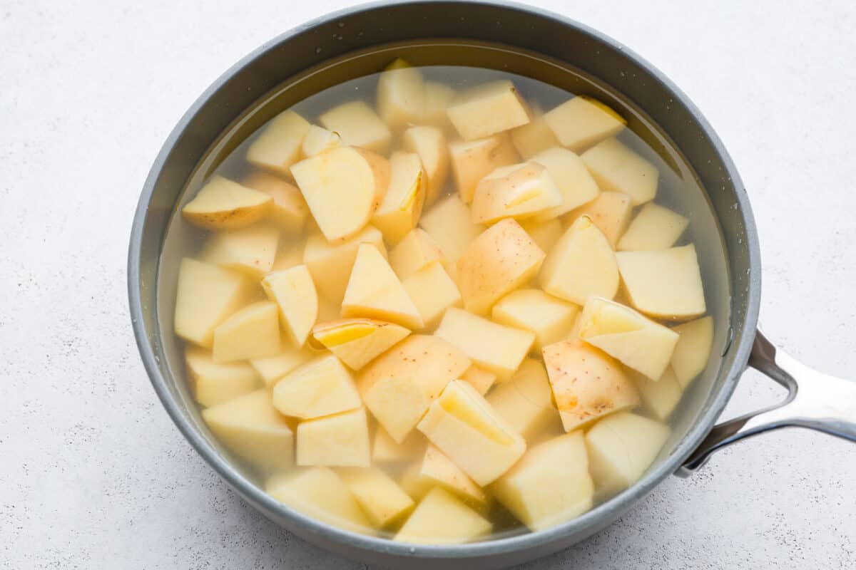 First process photo of the cut potatoes in a pot with water. Second process photo of the butter, cream, Boursin cheese, and spices. Third process photo of the ingredients added to the pot of boiled and drained potatoes. Fourth process photo of mashing the potatoes with the ingredients.