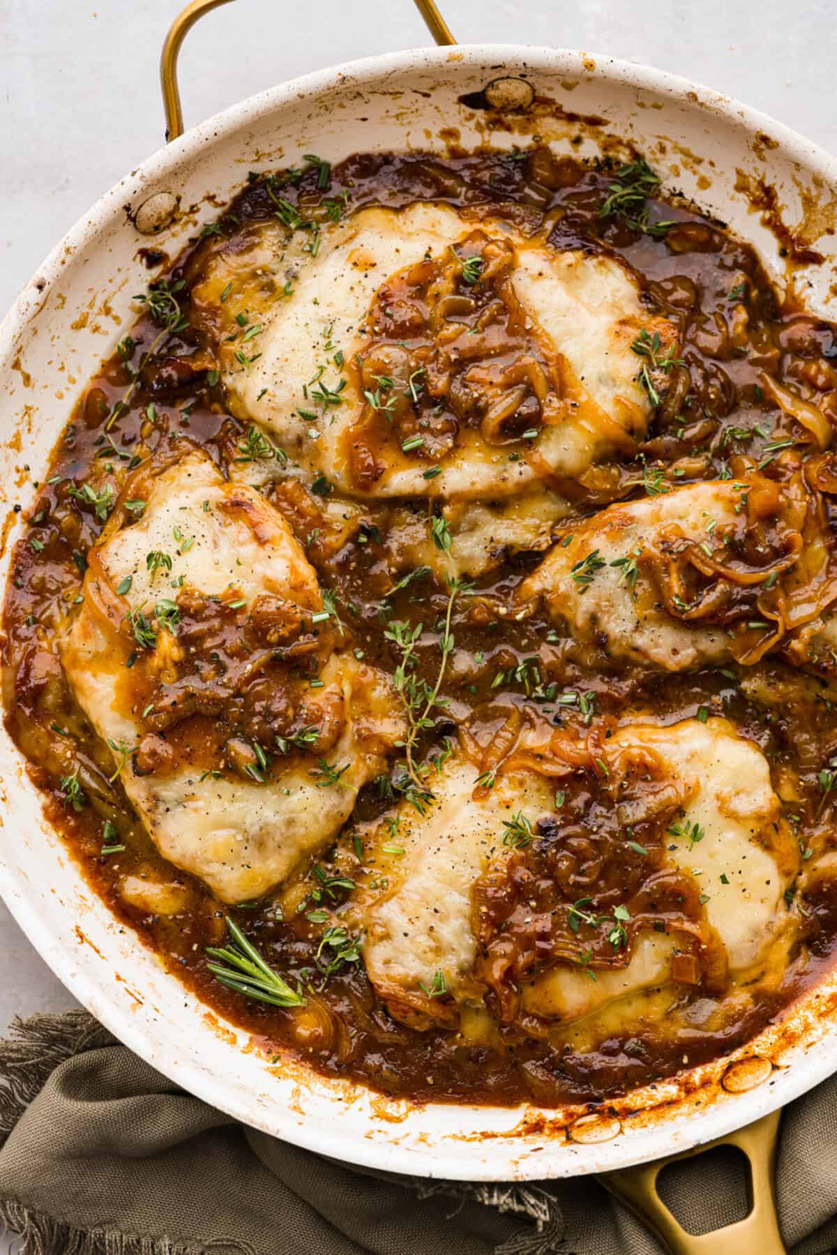 4 pork chops in a skillet topped with cheese and onion gravy.