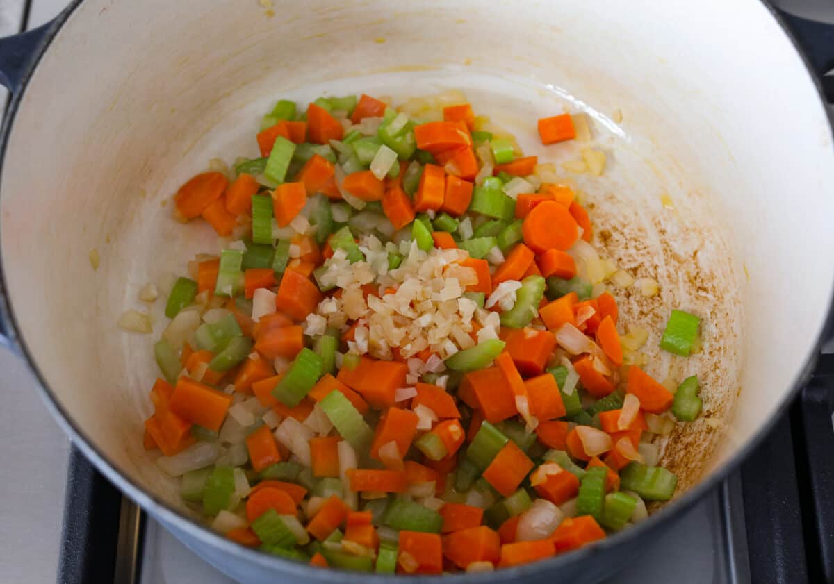 First process photo of the vegetables and garlic sautéing in a pot.