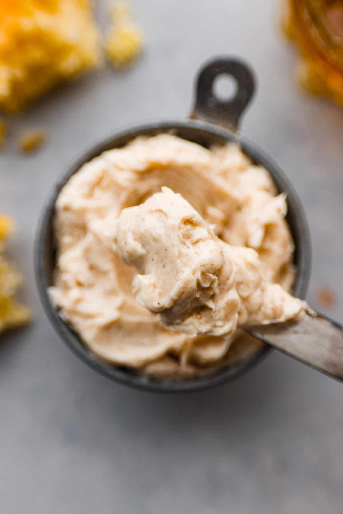 Closeup of a small bowl filled with honey butter, and a butter knife covered in it.