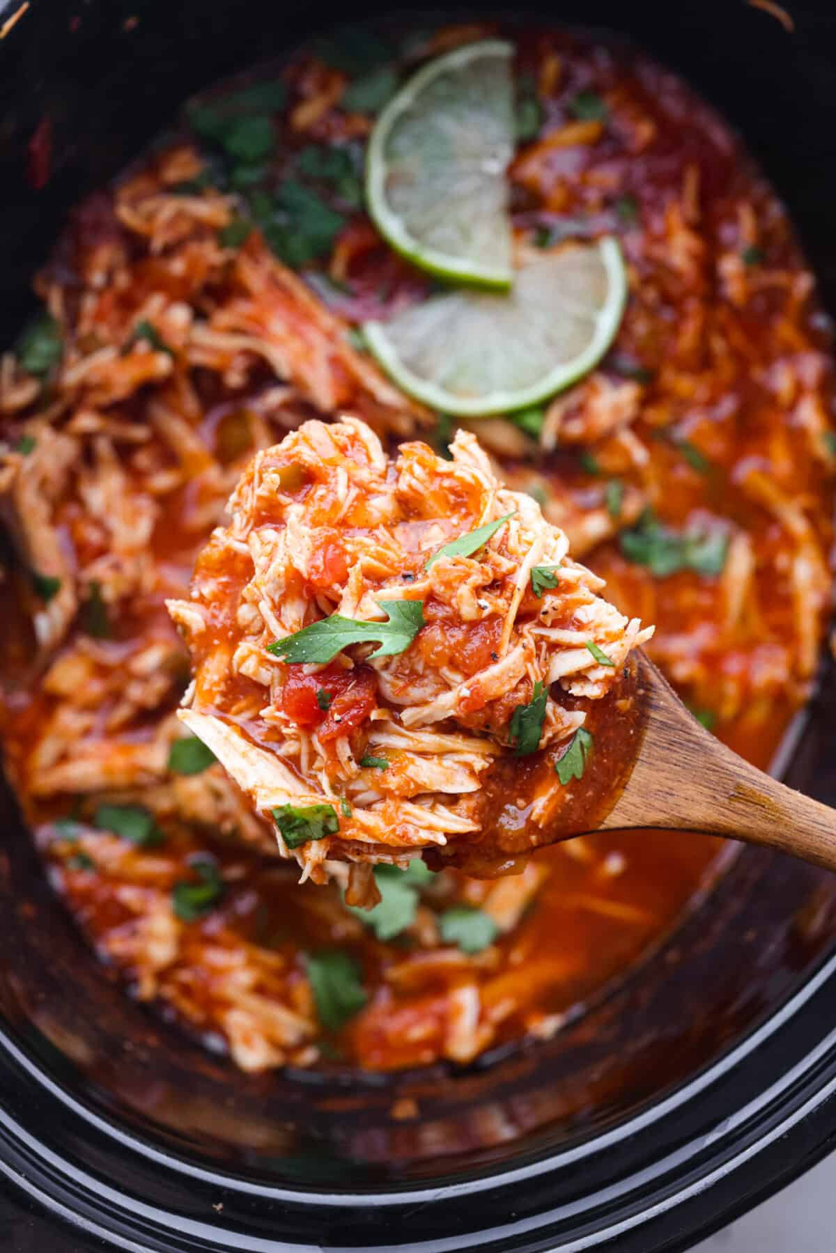 Close view of a serving spoon lifting chicken from the slow cooker.