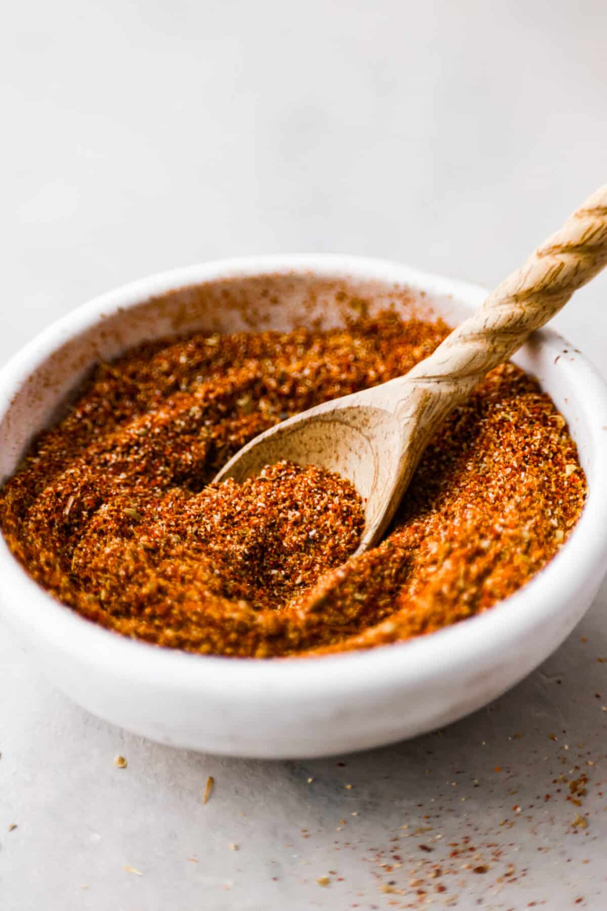 A white bowl of taco seasoning with a wooden spoon. 