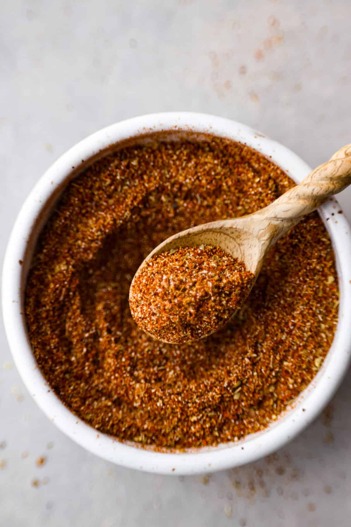 The top view of taco seasoning in a bowl with a wooden spoon scooping out some seasoning. 