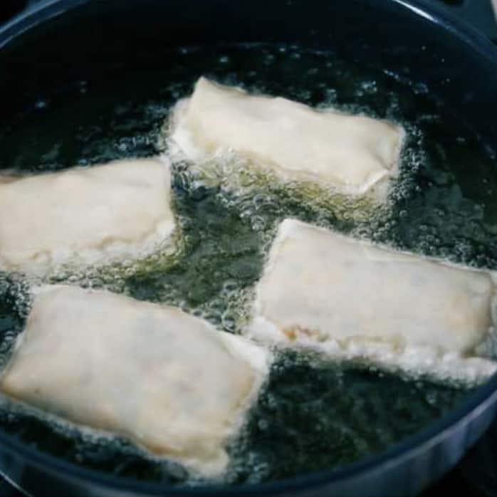 Fifth photo of the egg rolls placed in the hot oil to fry.