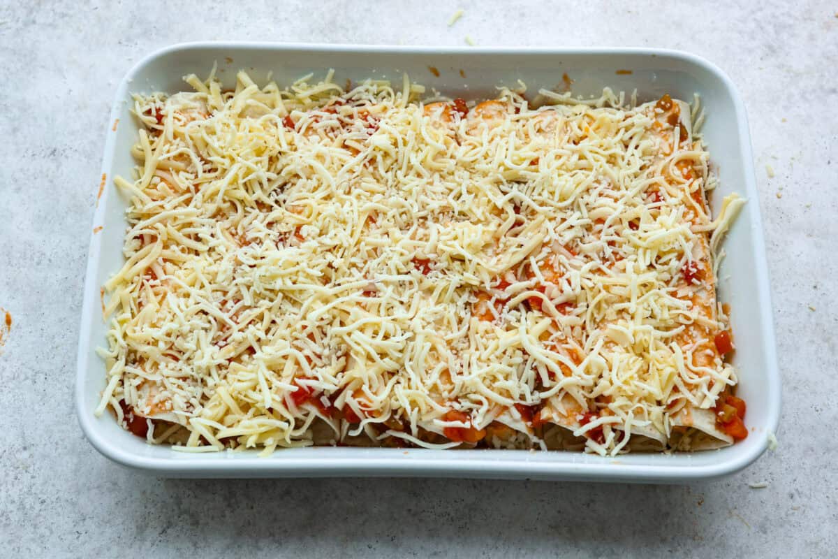 Eighth photo of the cheese sprinkled on top of the buffalo chicken enchiladas before baking.