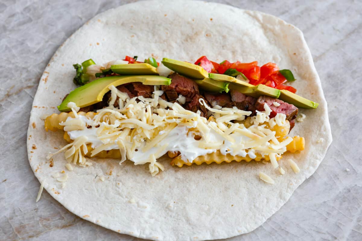 A tortilla being filled to make a California burrito. 