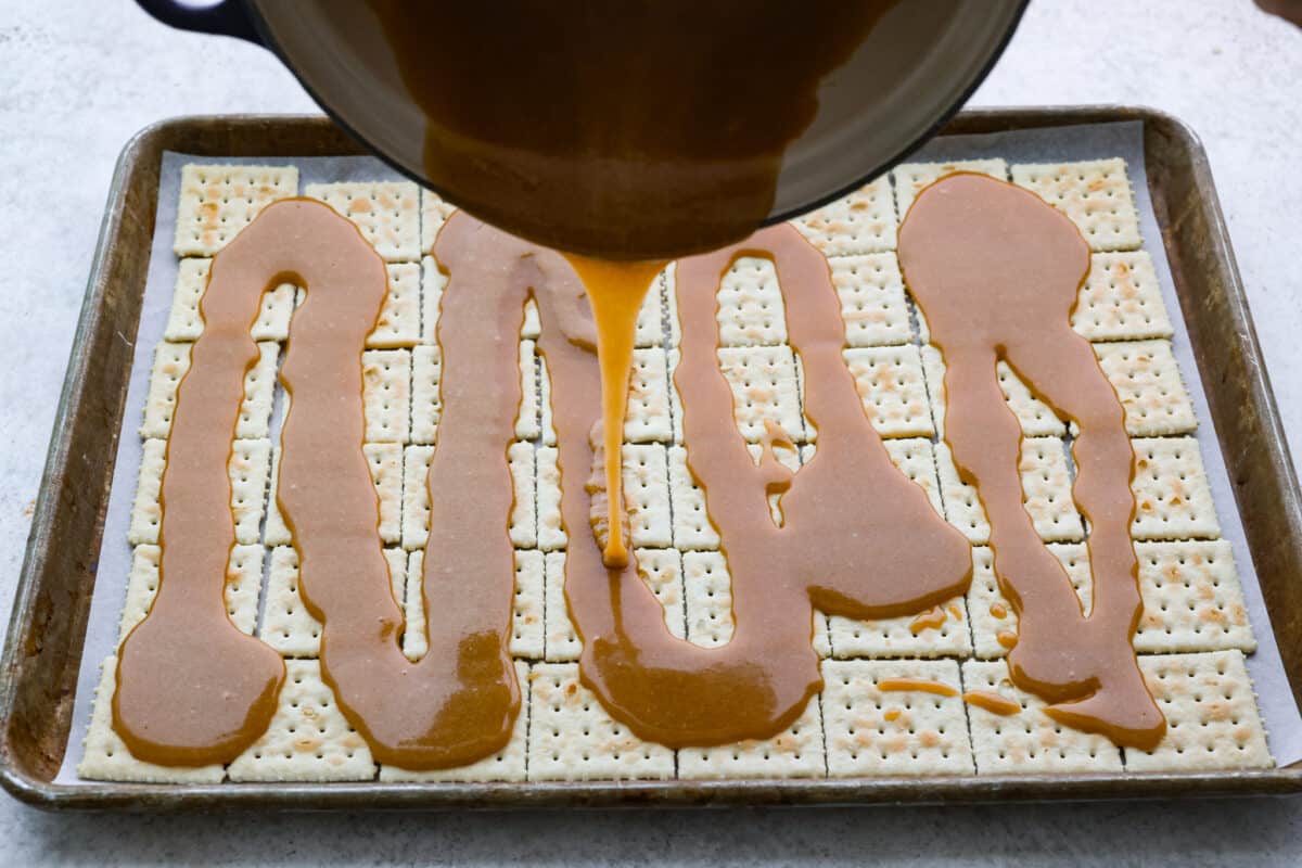 The brown sugar mixture being poured over saltine crackers. 