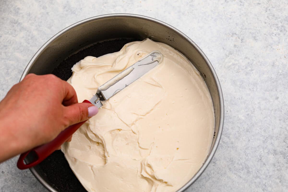 Overhead shot of someone smoothing cheesecake picture onto the Oreo crust in the springform pan. 