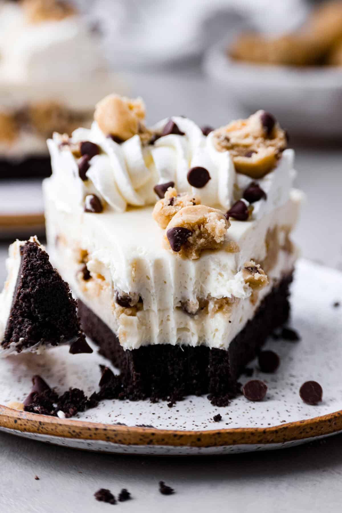 Close-up image of the front of a slice of the no-bake cookie dough cheesecake with a bite taken out of it which is sitting on a fork next to the slice. 