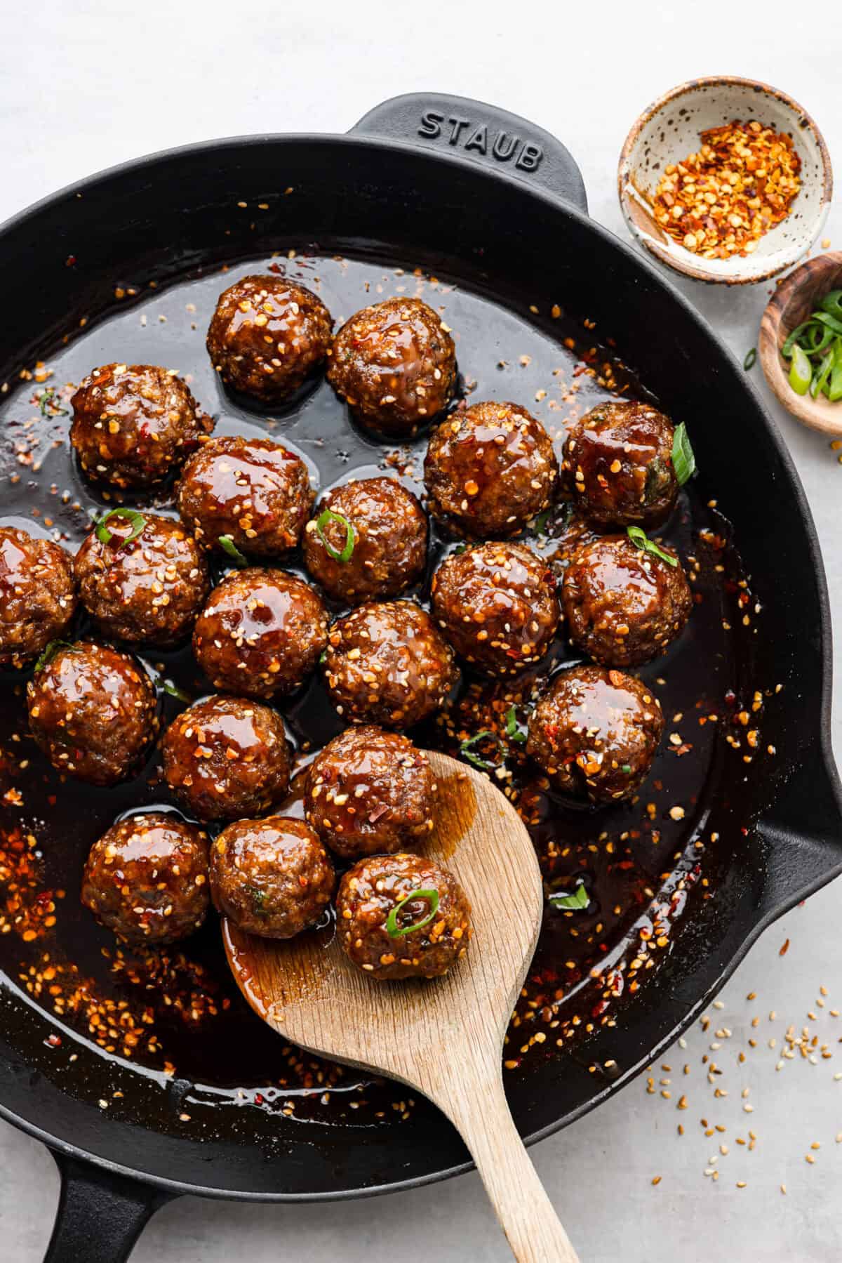 overhead shot of firecracker meatballs doused in sauce in a skillet with wooden spoon. 