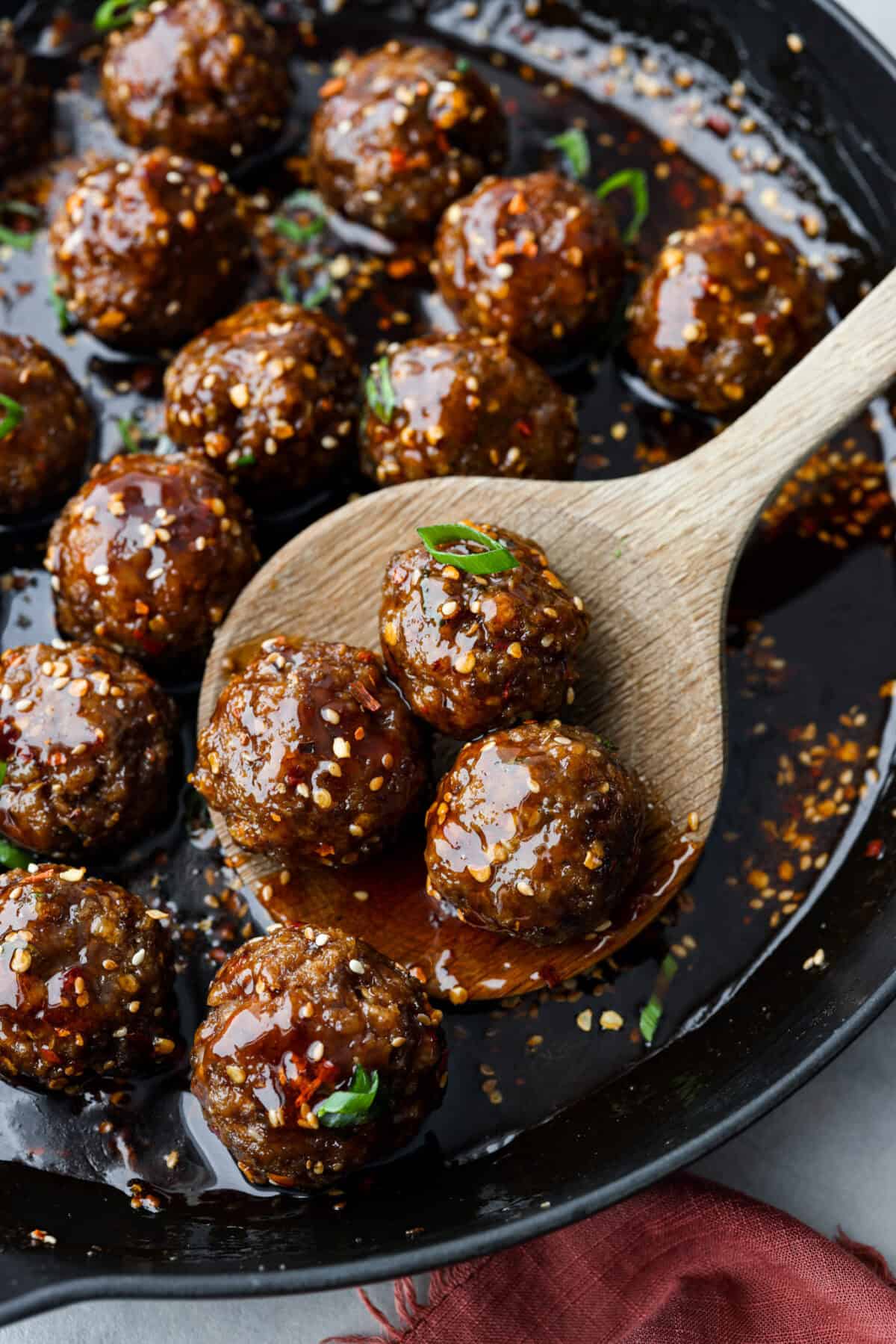 Close up shot of large wooden spoon scooping meatballs out of a  skillet. 