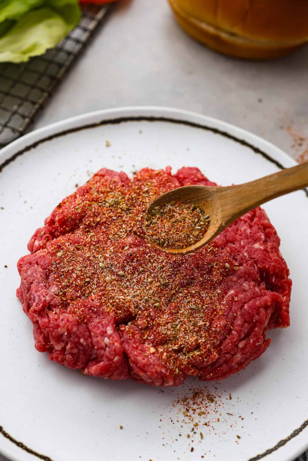 Burger seasoning being sprinkled on ground beef. 