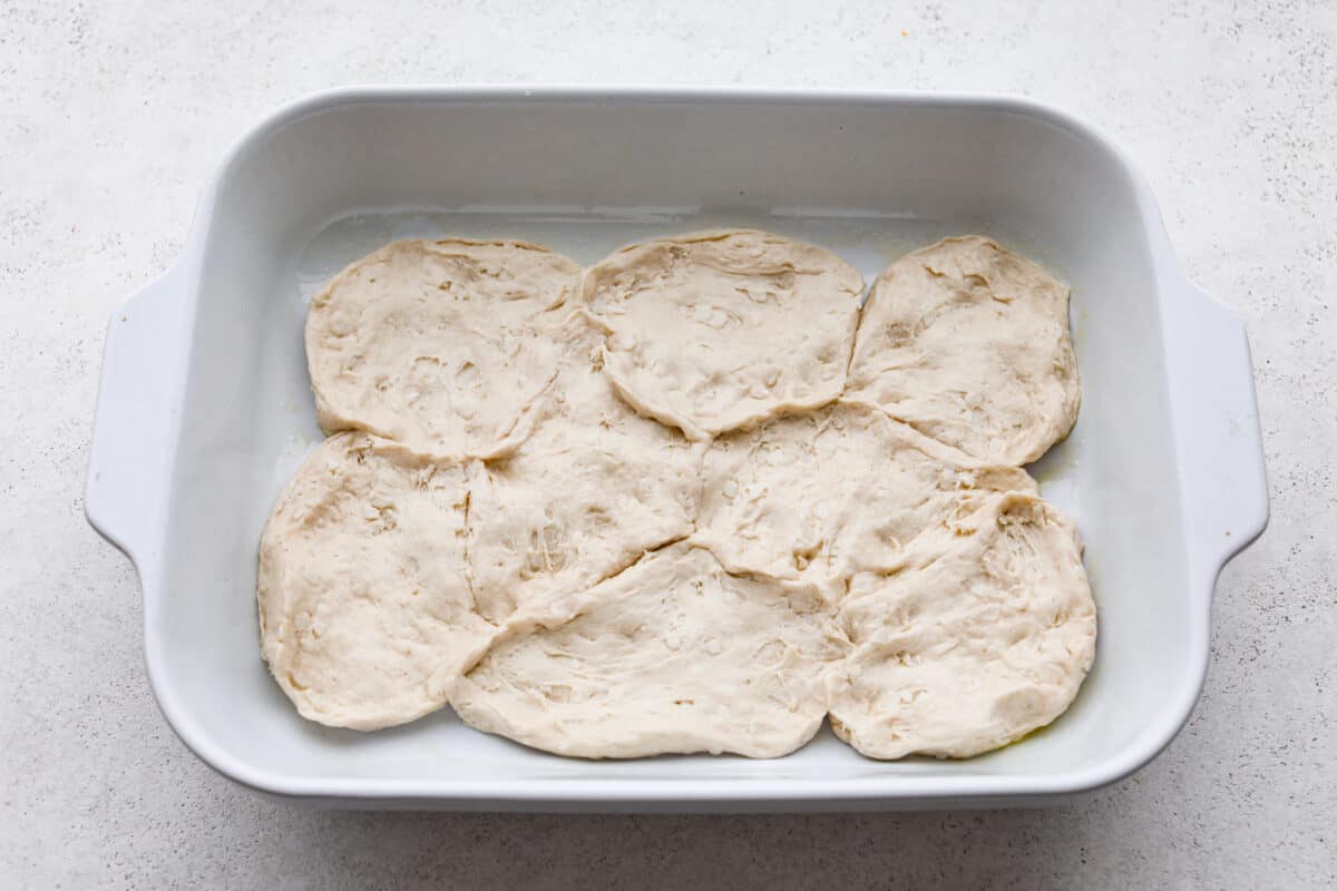 Grand biscuits being pressed a the bottom of a casserole dish for John Wayne casserole.