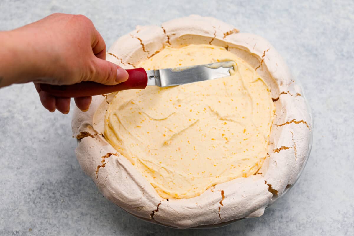 Fifth process photo of the lemon filling being spread into the meringue pie shell.