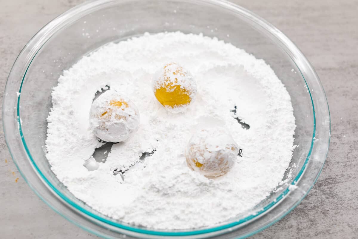 Rolling the unbaked lemon crinkle cookies in powdered sugar.