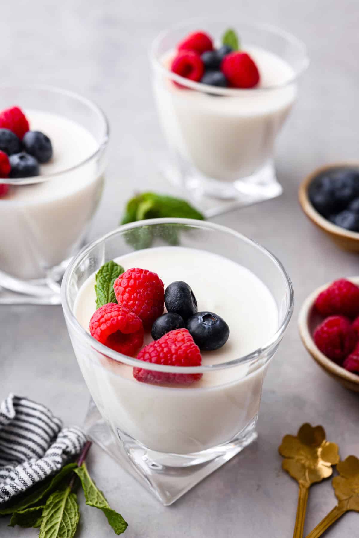 Angle shot of a glass cup with Swedish cream with raspberries, blueberries and a sprig of mint on top. 