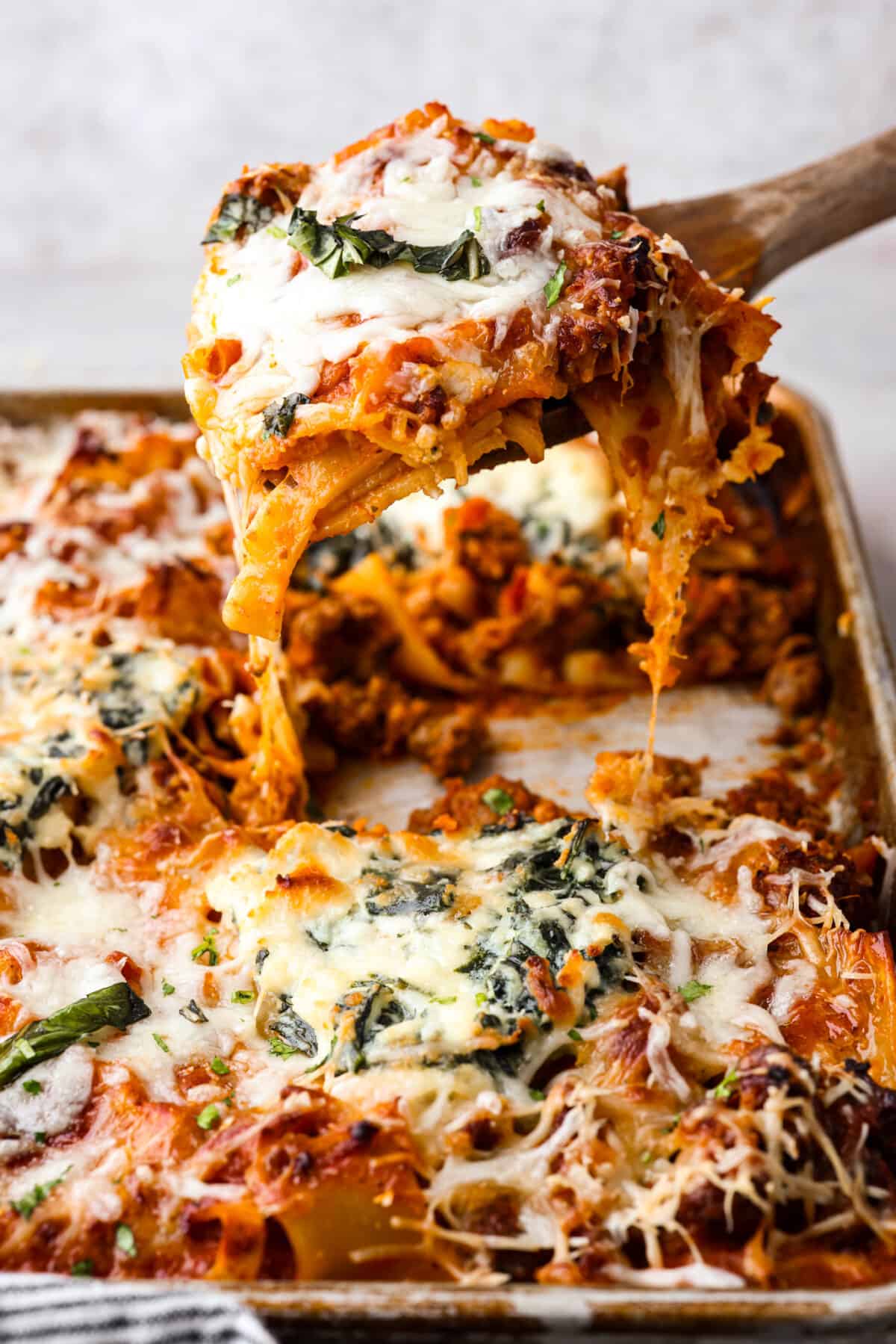 Sheet pan lasagna being served out of a sheet pan with a wooden spoon. 