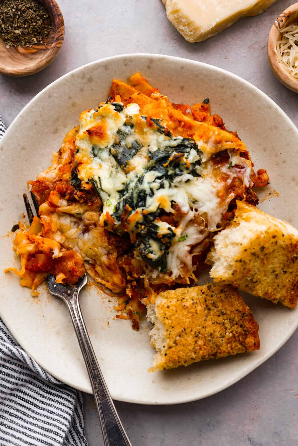 A small plate with a slice of lasagna and some garlic bread. 