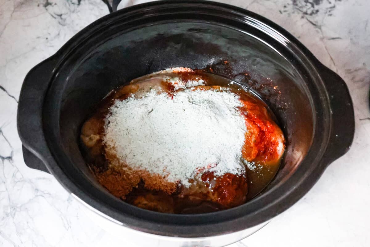 First process photo of the chicken and seasoning in the slow cooker.