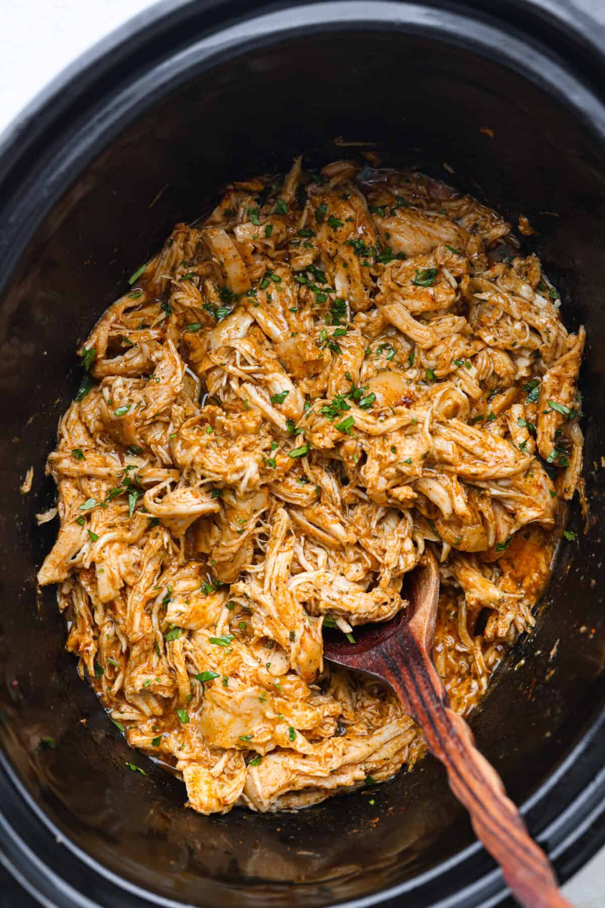 Top view of cooked in a slow cooker with a wooden spoon and cilantro garnished on top.