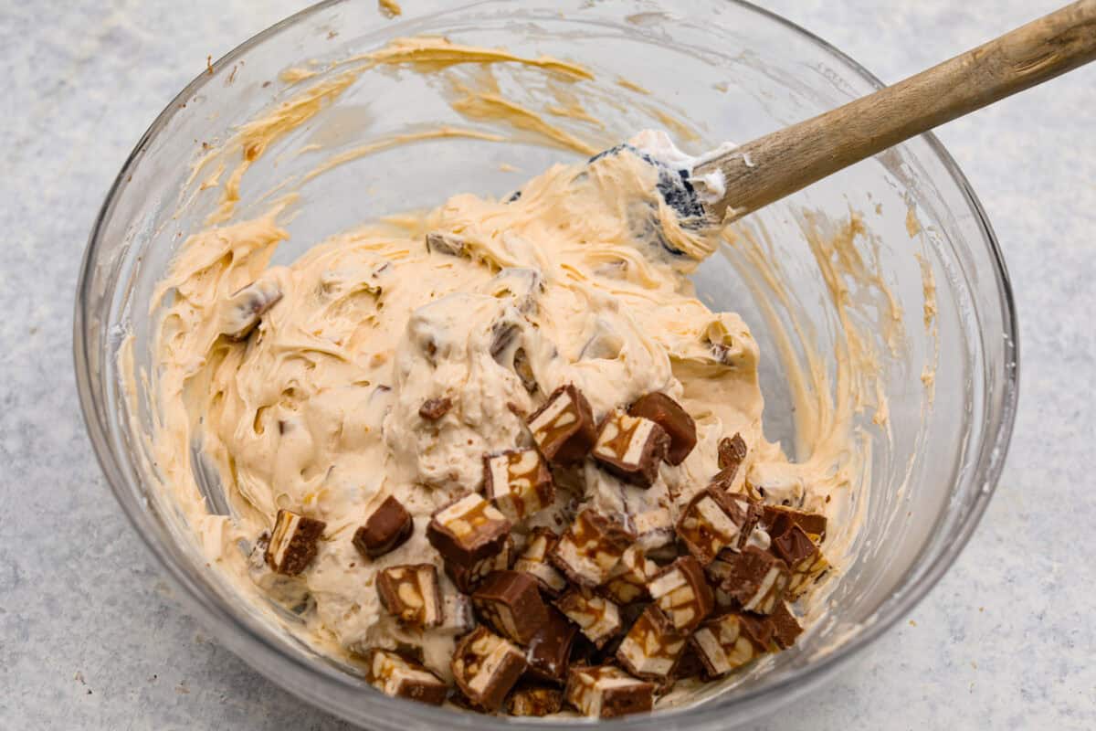 Chopped snickers bar being added into the glass bowl of filling for the no bake snickers bar pie. 