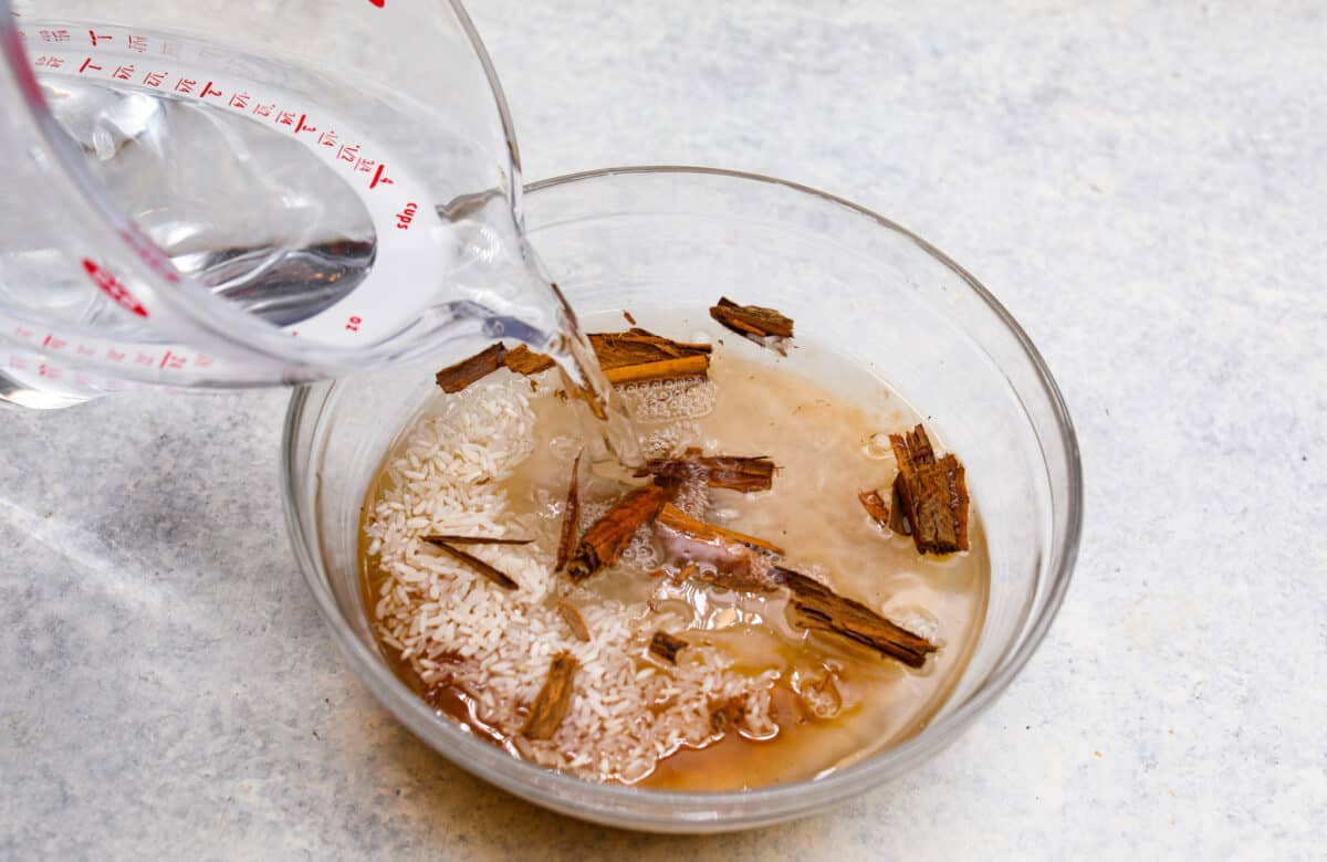 Process photo of water pouring into a bowl of rice and cinnamon sticks.