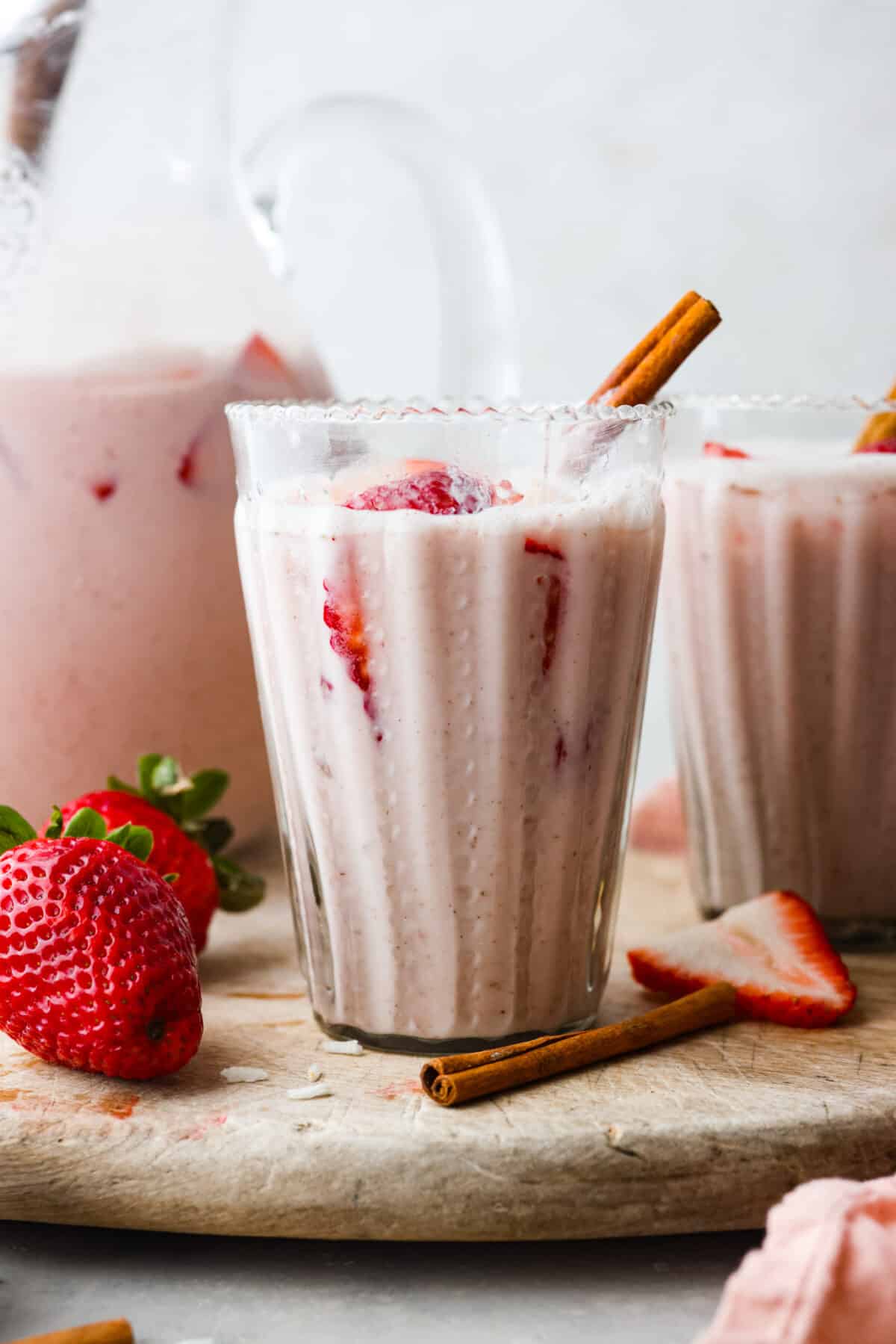 Close view of a glass of strawberry horchata with a pitcher behind it. 