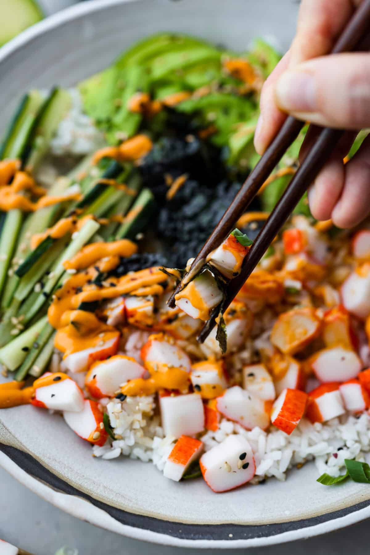 Close up shot of someone taking a bite of the sushi bowl with chopsticks.  