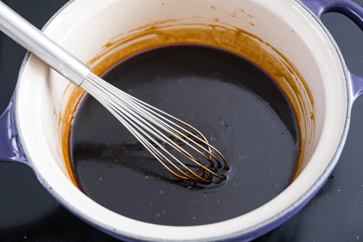 A sauce pan with teriyaki sauce and a whisk. 