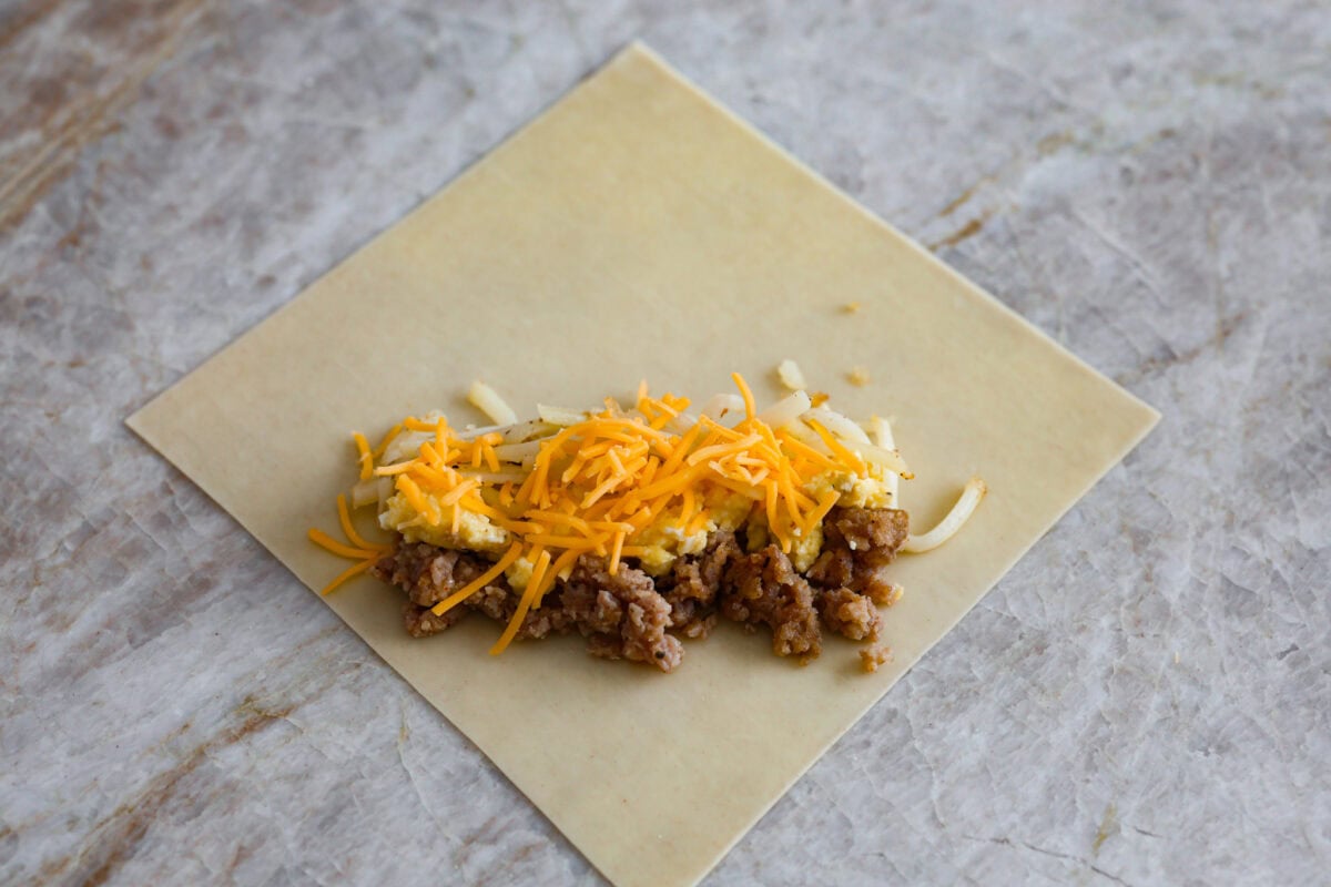 Overhead shot of egg roll paper open with ingredients for breakfast egg rolls on top. 