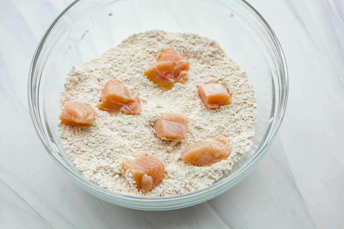 Raw chicken being coated with the dry ingredients in a glass bowl. 