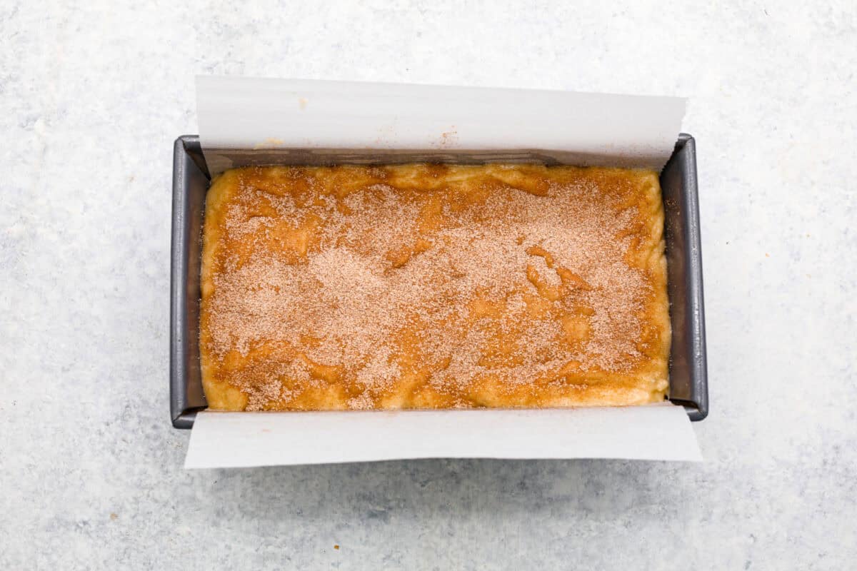 Overhead shot of batter in bread pan covered in cinnamon and sugar. 