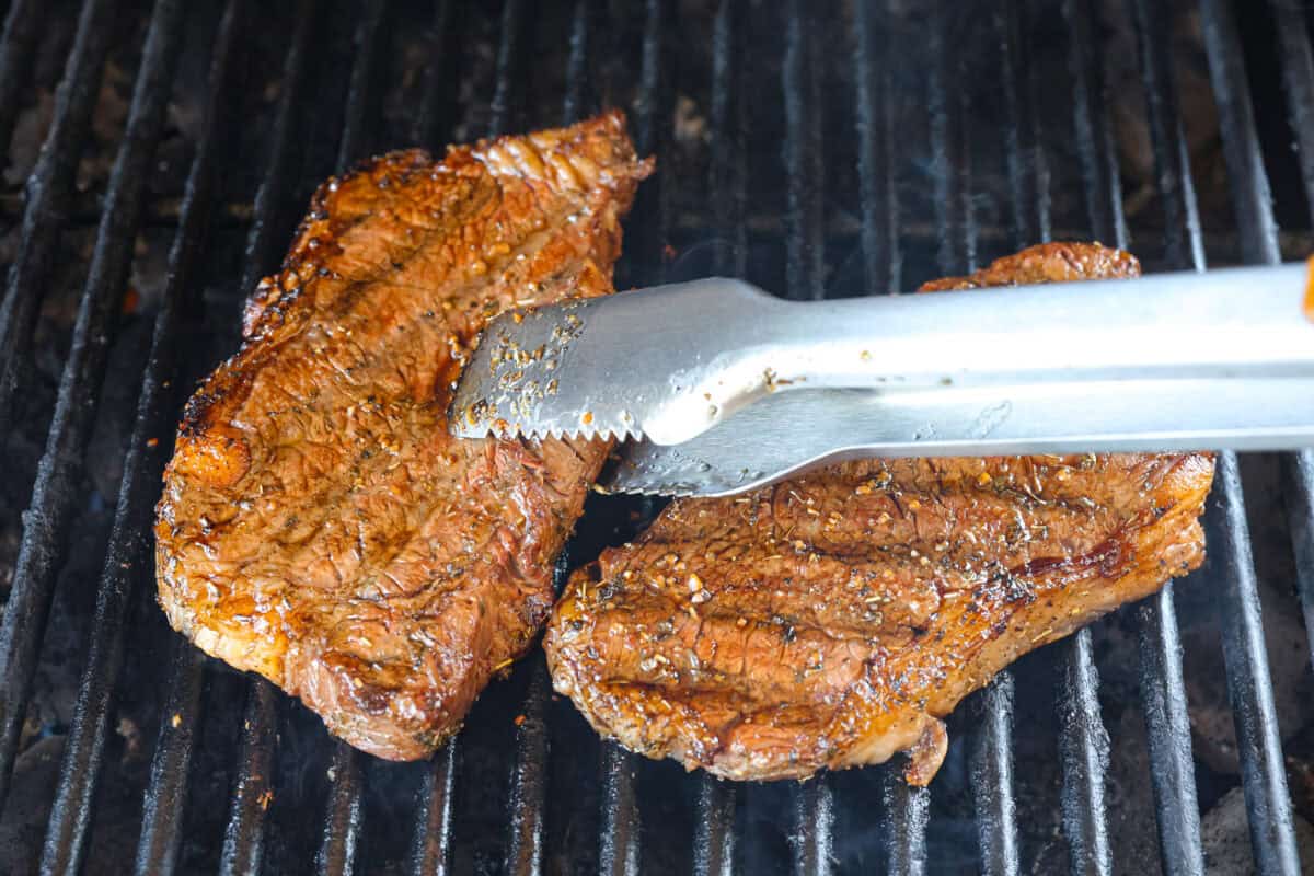 First photo of tongues flipping the steak.