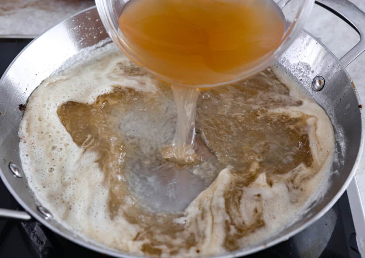 Beef broth being added into a pan. 