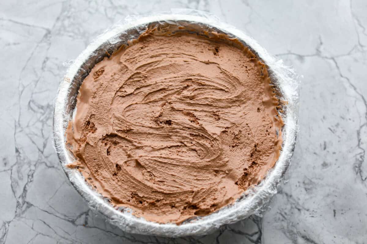 Overhead shot of smoothed out ice cream layers in plastic wrapped bowl. 