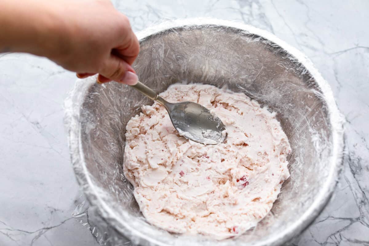 Overhead shot of ice cream being spread into the bottom of a plastic wrapped bowl. 