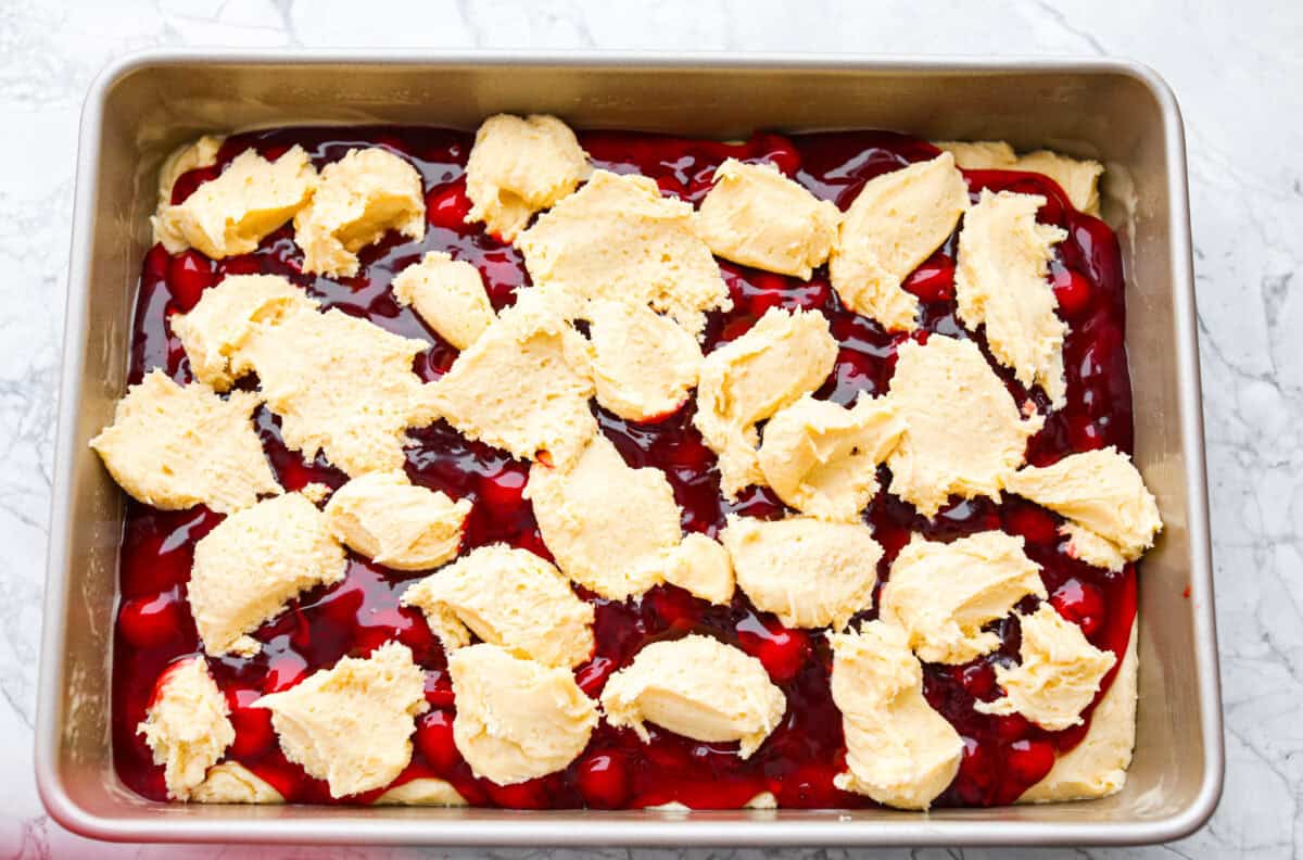 Remaining batter being spooned on top of the pie filling just before baking the cherry pie bars. 