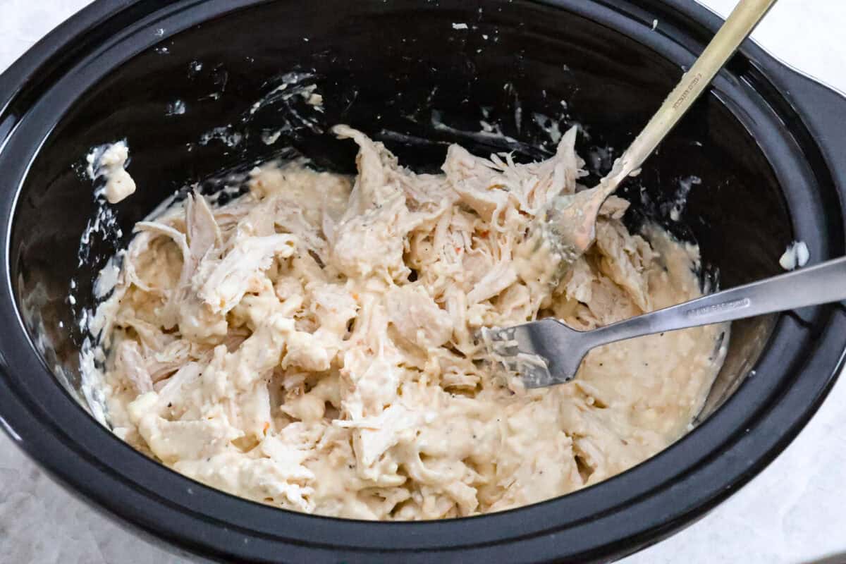 Overhead shot of cooked chicken being shredded in crock pot with two forks. 