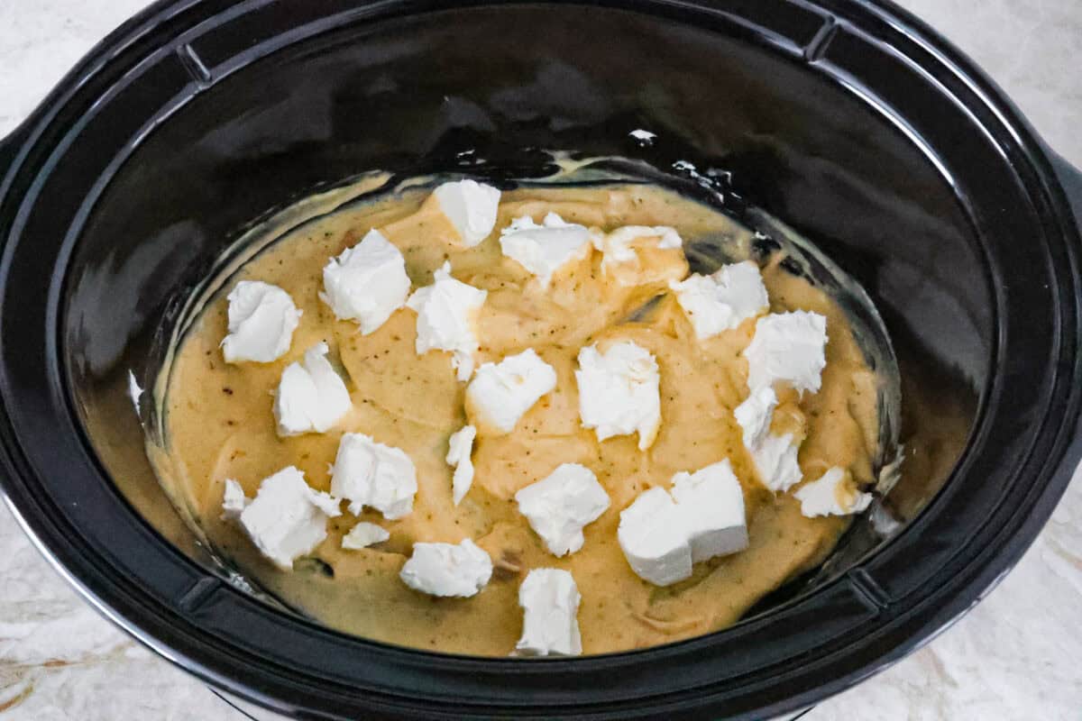 Overhead shot of canned cream of chicken soup mixed with Italian seasoning with cubed cream cheese on top. 