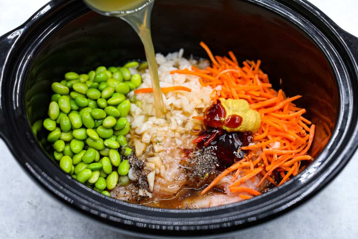 Overhead shot of broth being poured in to a crockpot full of ingredients. 