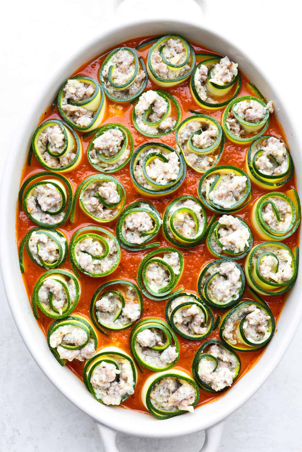 Overhead shot of zucchini rolls in marinara sauce in pan. 