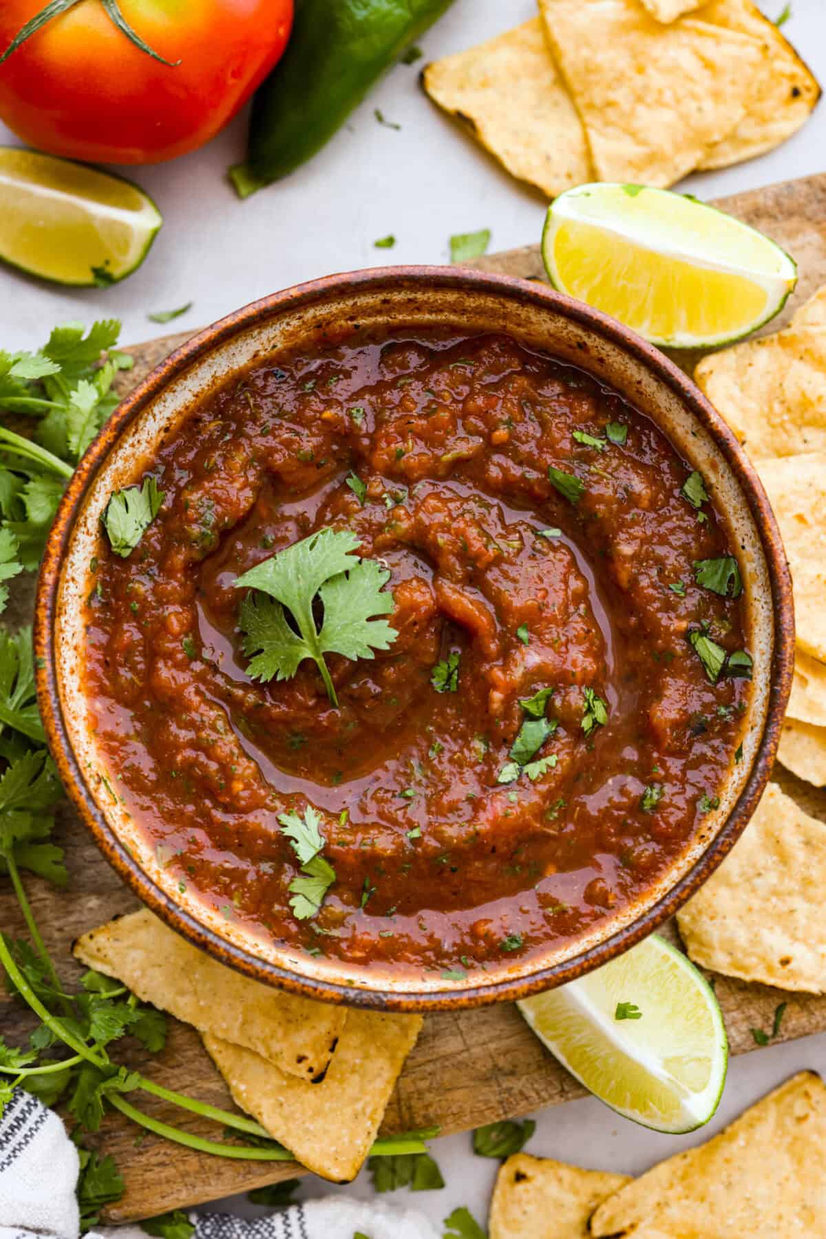 Overhead shot of bowl of blender salsa surrounded by limes, tortilla chips and fresh cilantro. 