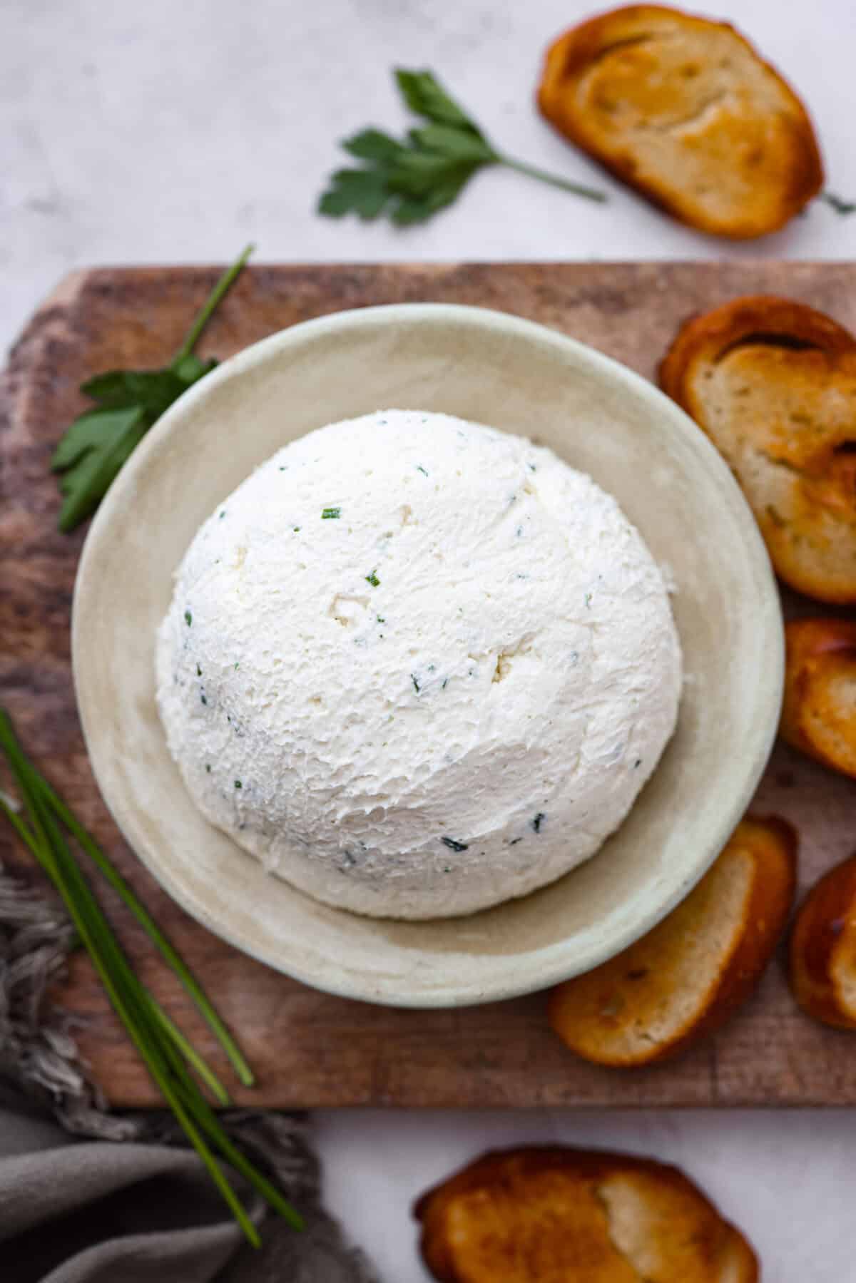 Overhead shot of Boursin cheese ball on plate next to crostini's and chives.